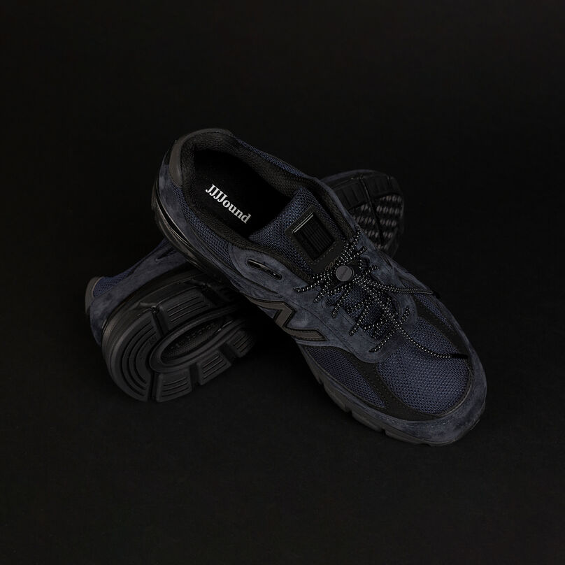 Une paire d’espadrilles NB 990v4 bleu marine sur un fond de studio gris foncé.