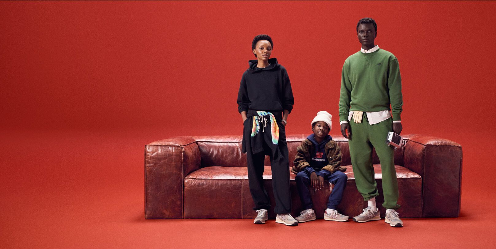 Famille de trois assise sur un canapé en cuir rouge sur fond rouge.