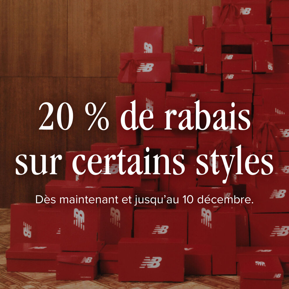 Une grande pile de boîtes à chaussures New Balance rouges avec des arcs rouges attachés en hauteur contre un mur de panneaux de bois
