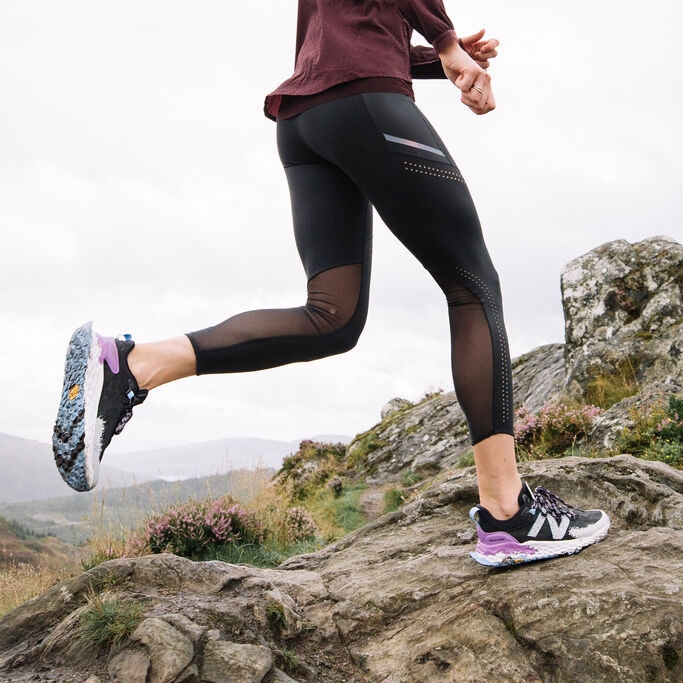 Woman running on rocky mountainous terrain in the black and purple Hierro v5