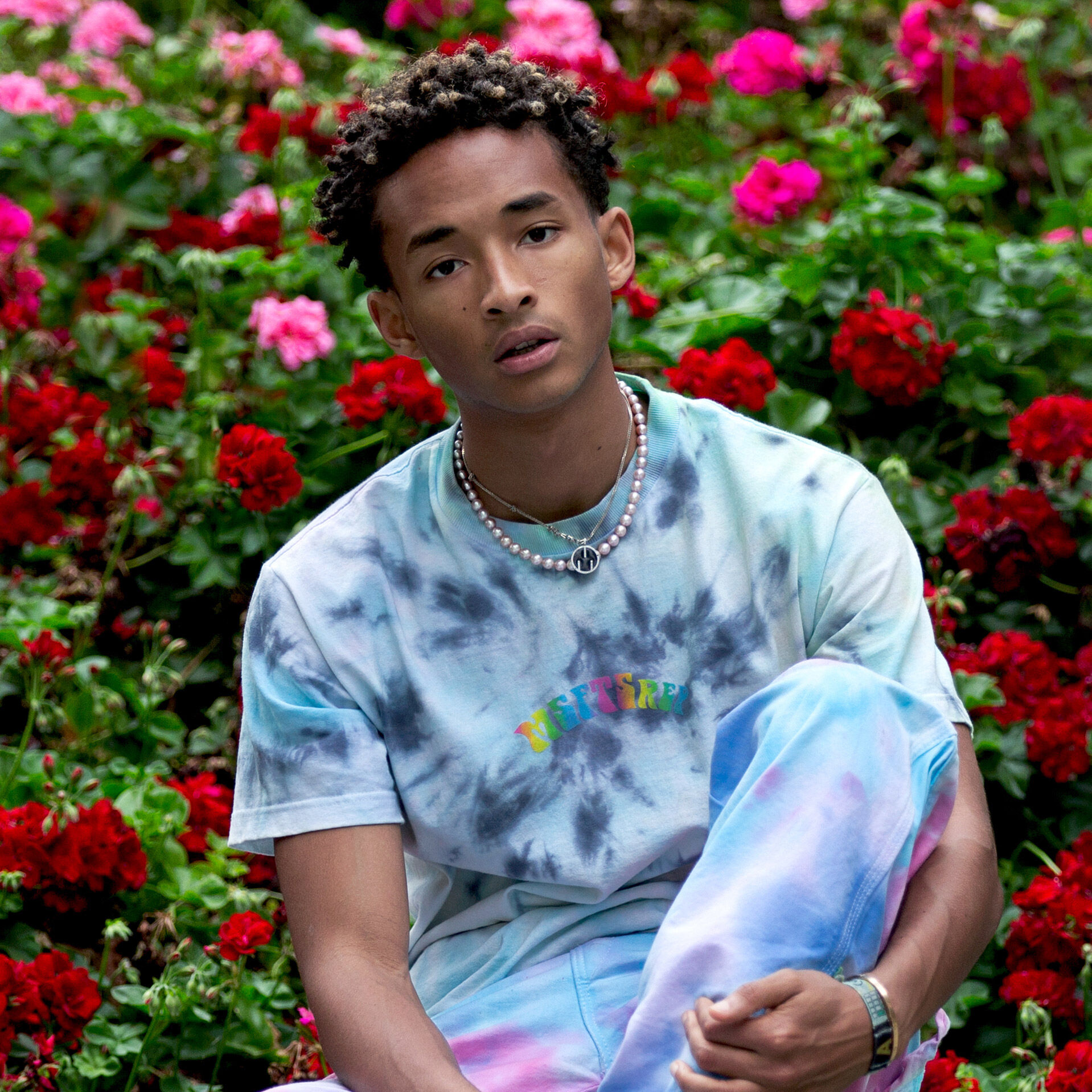 Jaden Smith in tie-dye outfit sitting in front of flowers