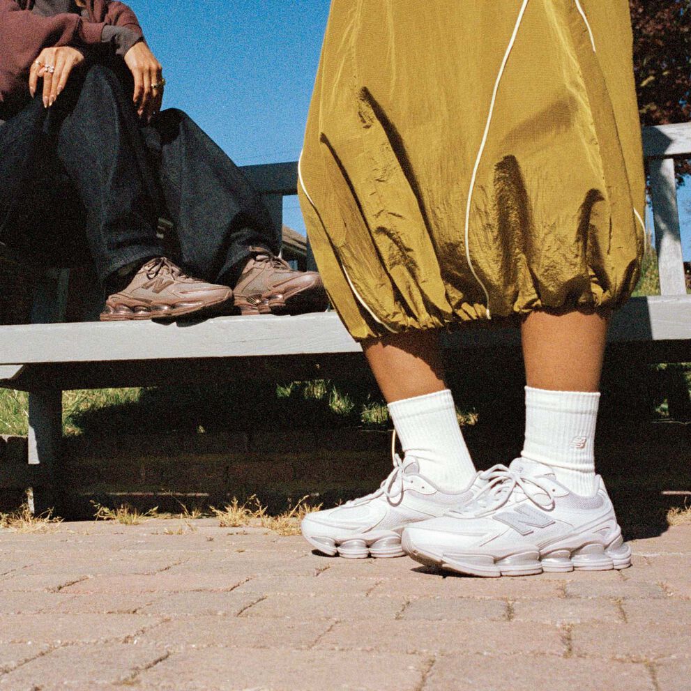 Knee-down of two people wearing New Balance sneakers outside.
