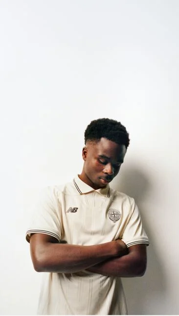 Saka looking down with his arms folded wearing a beige jersey.