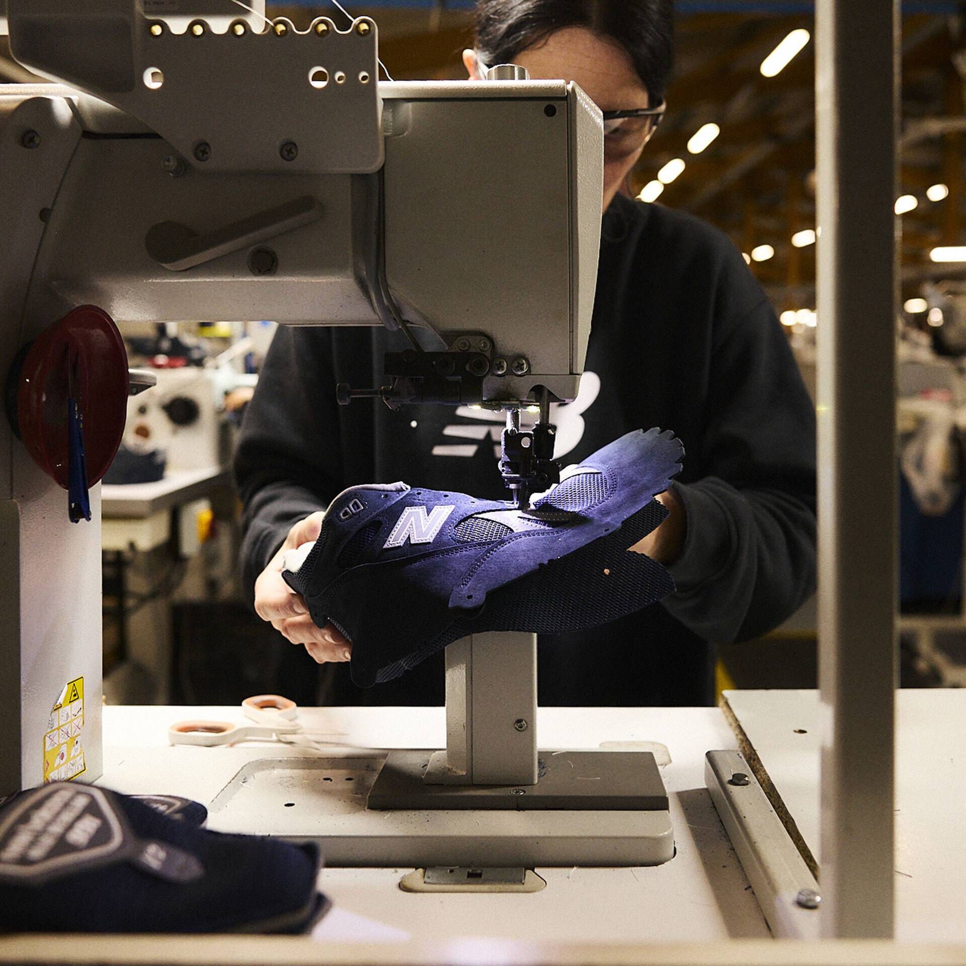 A person stitching a shoe in a factory setting.
