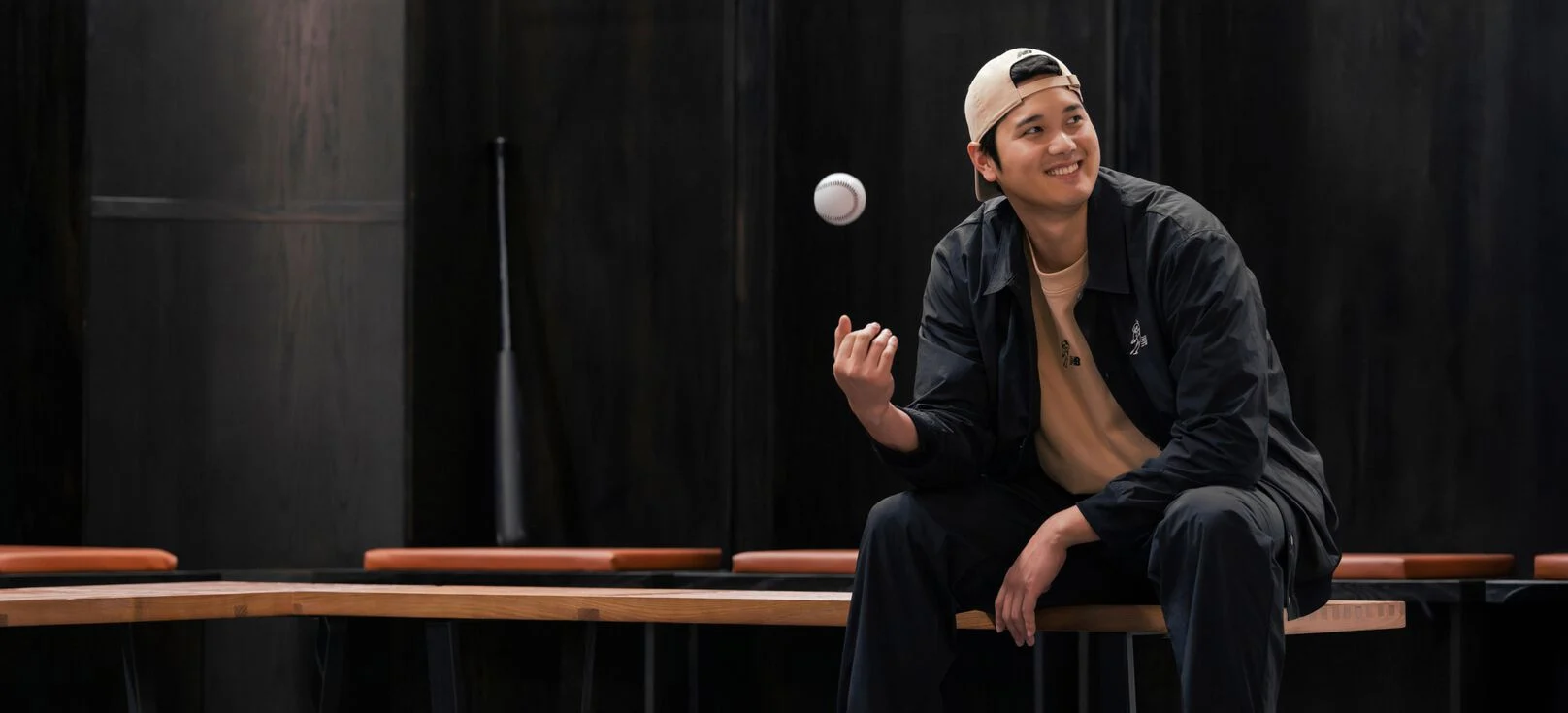 Ohtani assis dans un vestiaire lançant une balle dans les airs.  