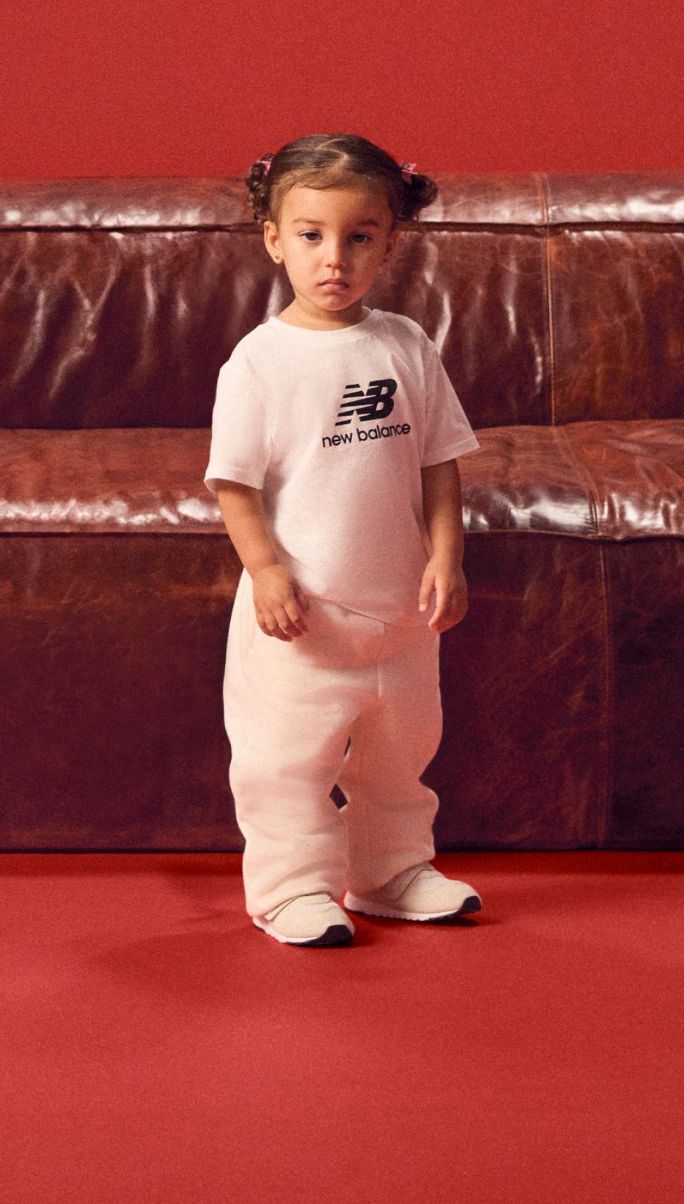 Bébé en tenue blanche debout devant un fond rouge.