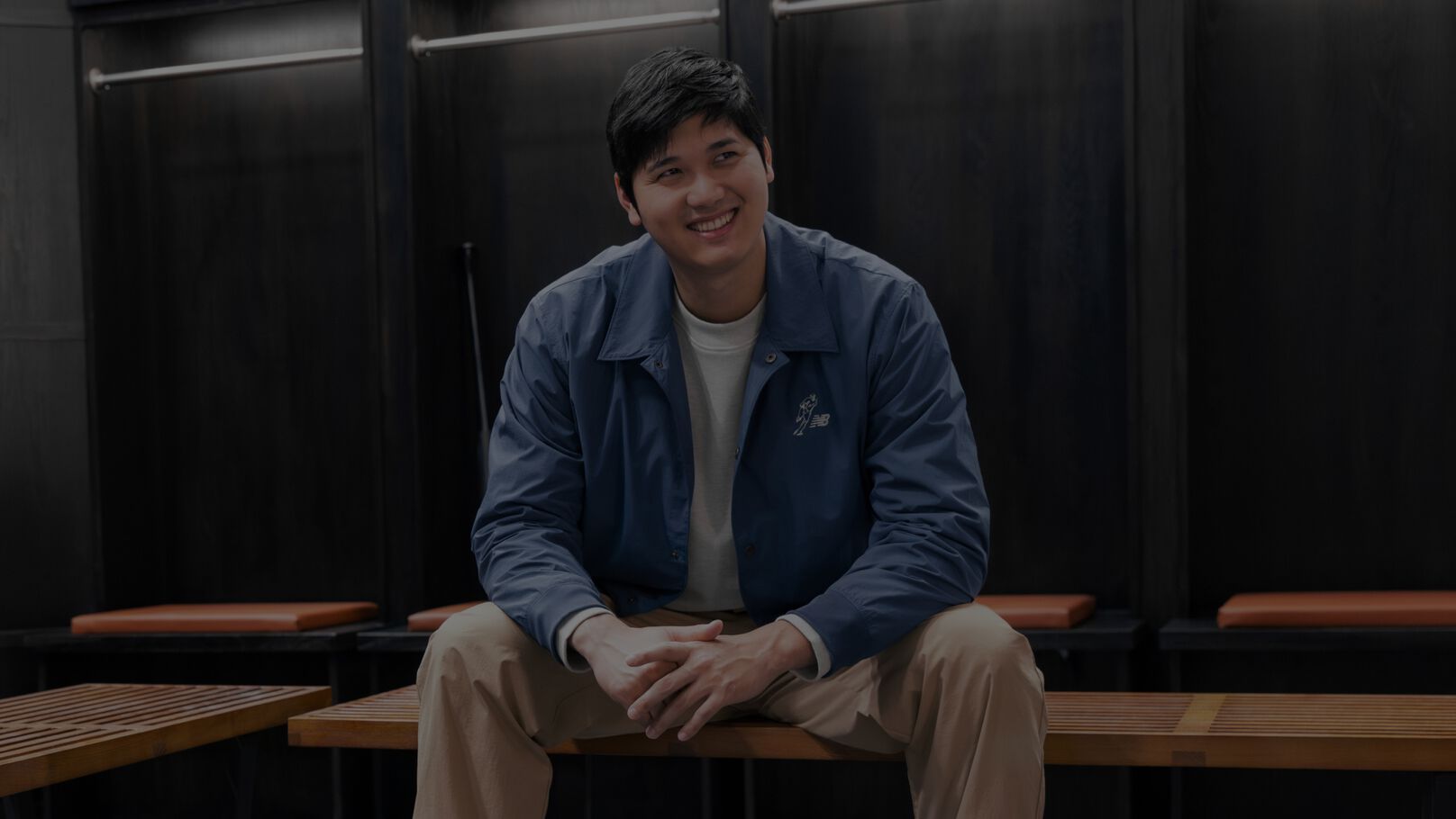 Shoehei Ohtani assis dans un vestiaire en veste bleue.