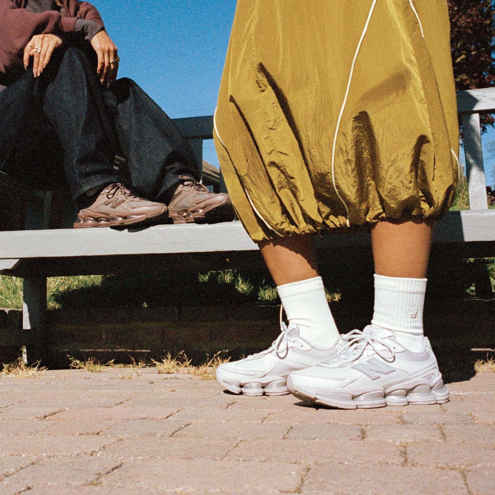 Knee-down of two people wearing New Balance sneakers outside.
