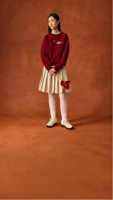 Femme debout avec une jupe beige tenant des fleurs.