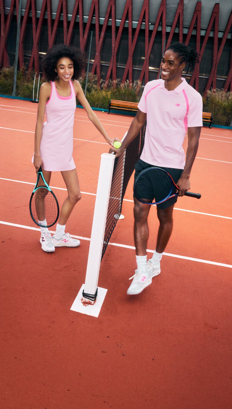 Des gens debout devant un filet de tennis sur un court en terre battue, v&ecirc;tus de v&ecirc;tements de tennis roses et de baskets, tenant des raquettes.