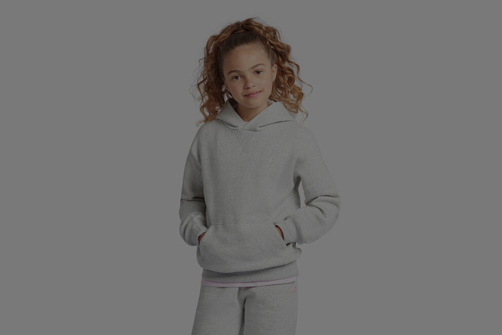 Fille en chandail à capuchon New Balance gris et pantalon de survêtement assorti.