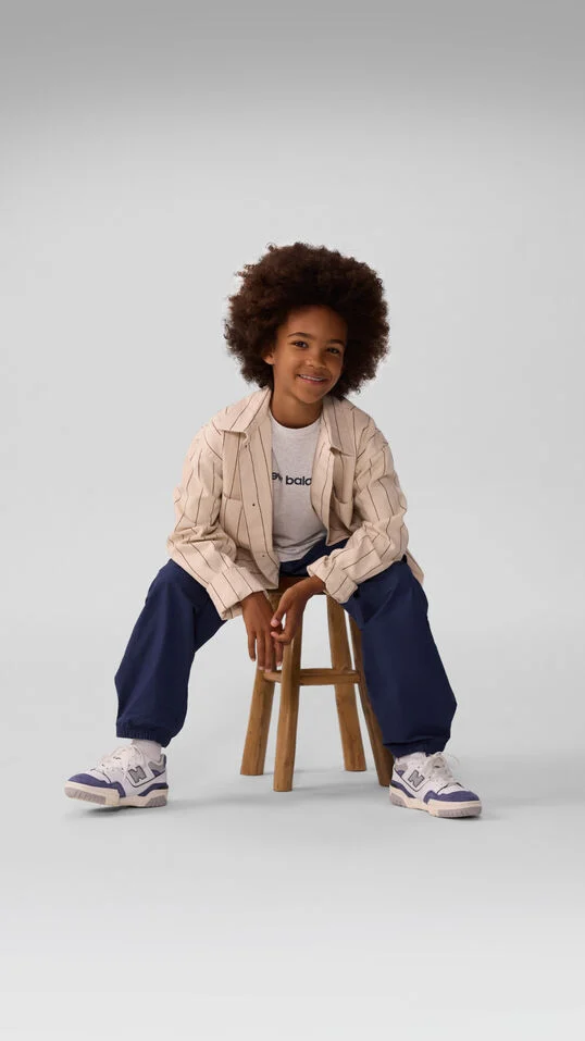 Jeune enfant assis sur un tabouret et portant un pantalon bleu. 