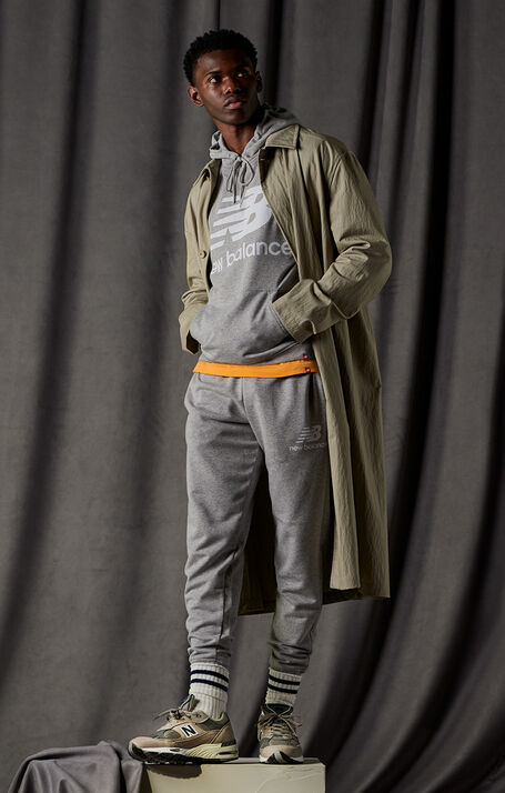 Man posing wearing a grey NB Essentials hoodie, grey NB Essentials joggers, and warm grey NB 991 sneakers