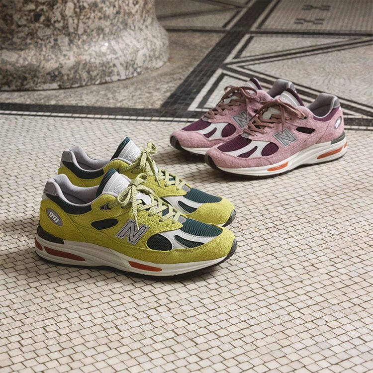 Two pairs of New Balance Made in UK sneakers on a textured white tiled floor.  