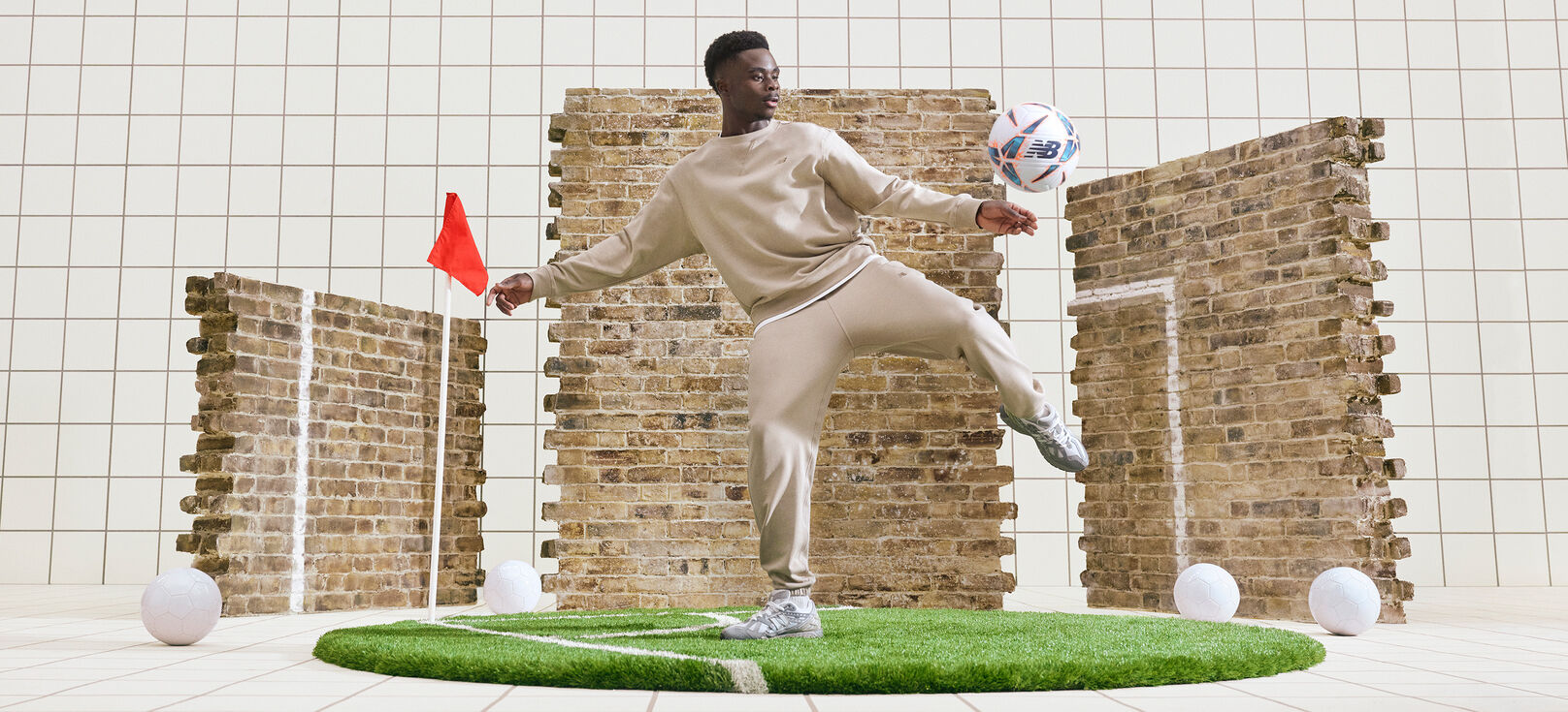 Bukayo Saka kicking a ball in front a brick wall.
