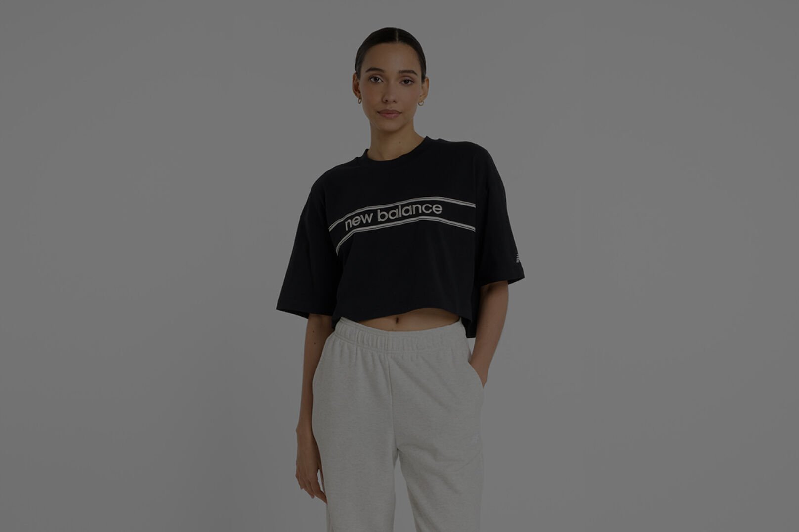 Femme portant un maillot New Balance noir et un survêtement New Balance gris.