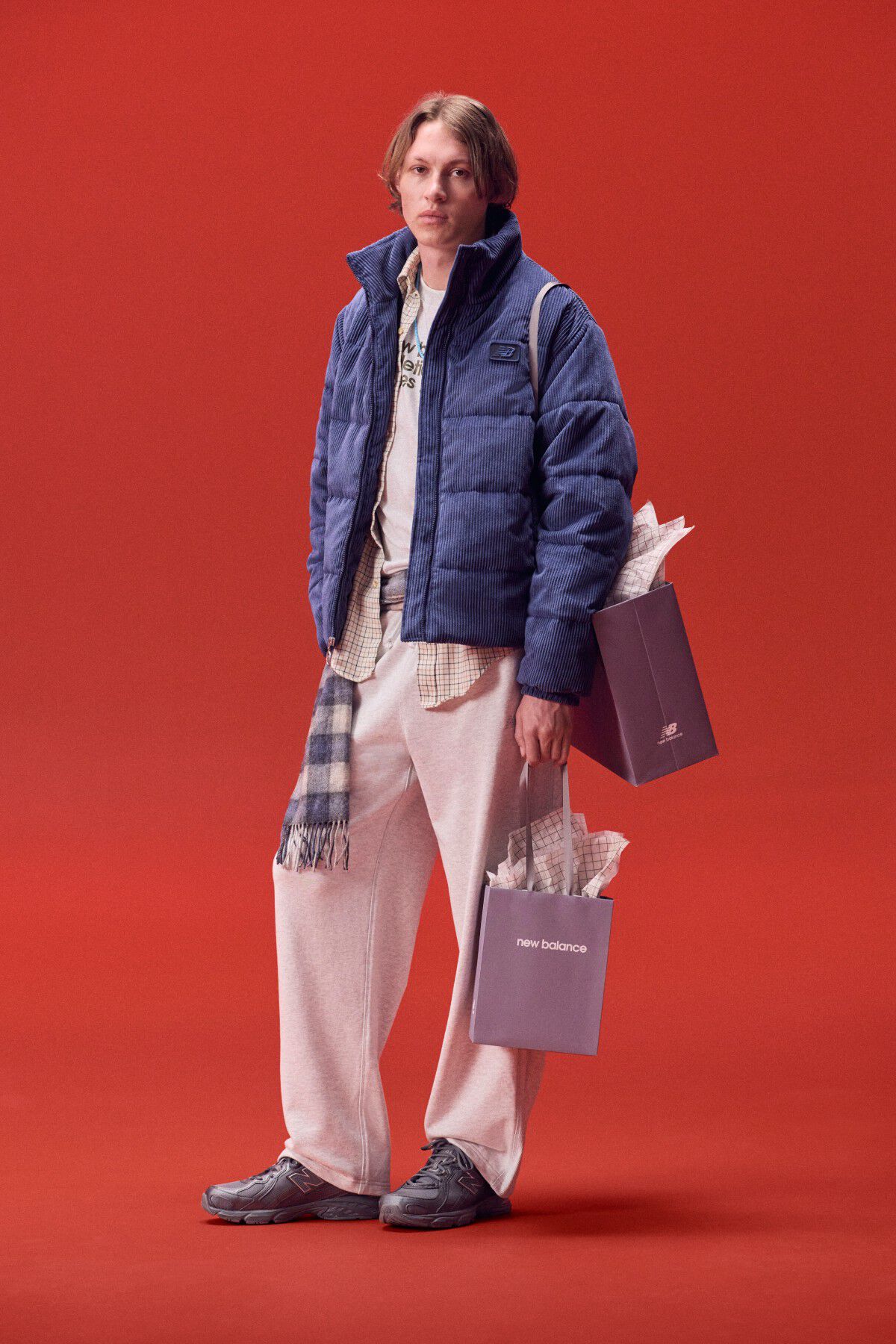 Jeune homme en veste bleue portant un sac de cadeaux sur fond rouge.