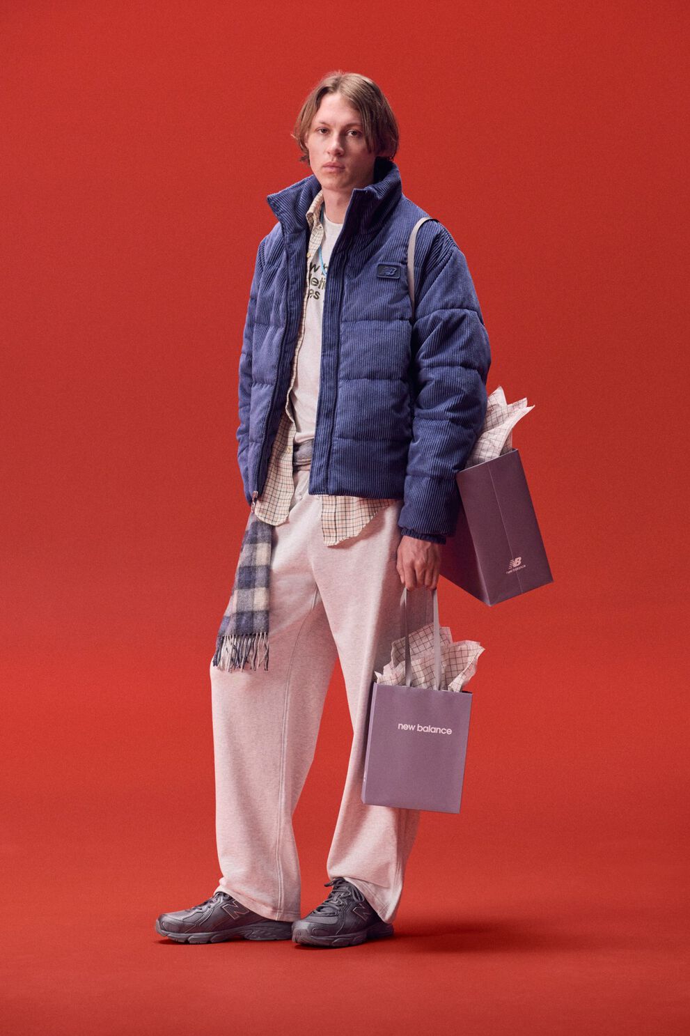 Jeune homme en veste bleue portant un sac de cadeaux sur fond rouge.