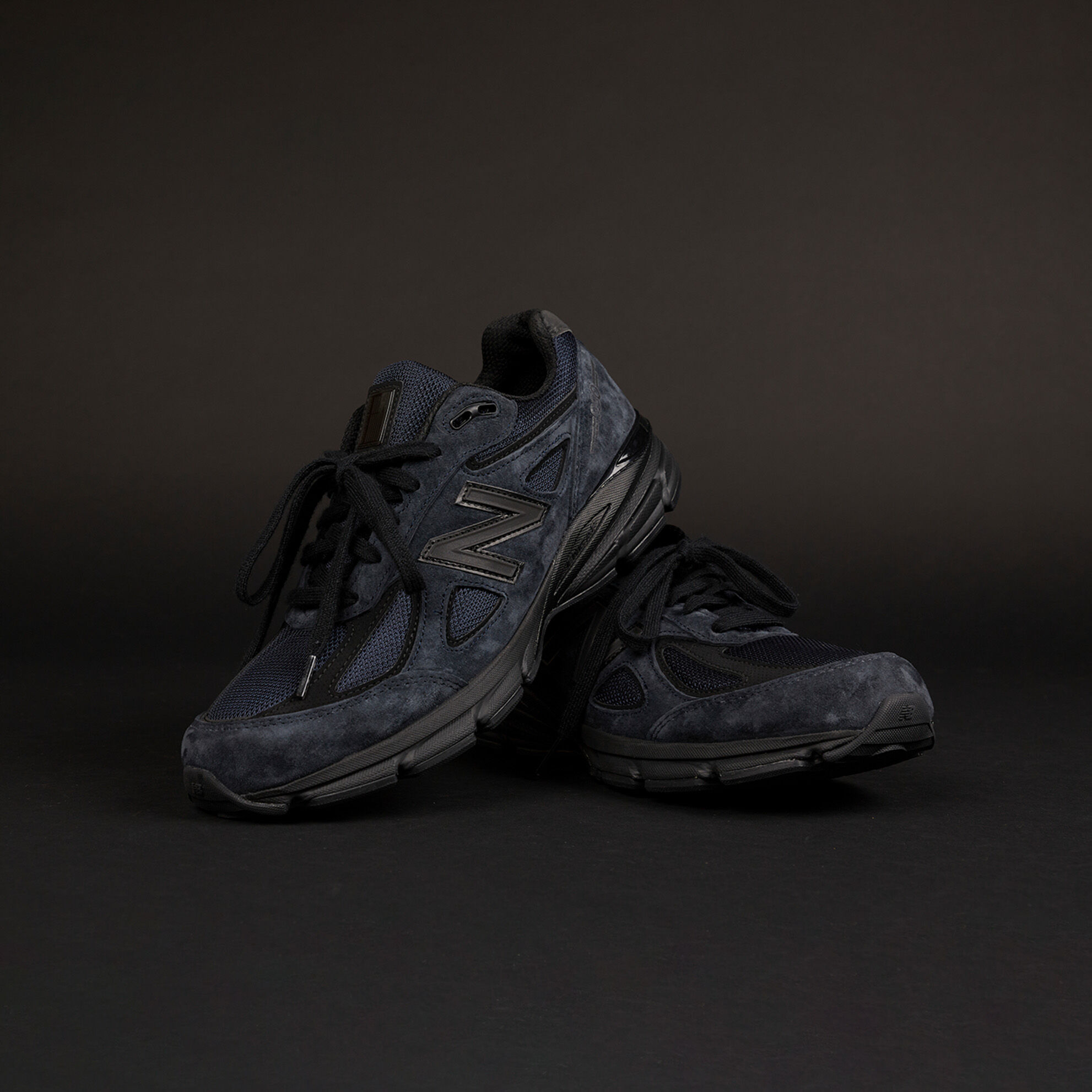 Une paire d’espadrilles NB 990v4 bleu marine sur un fond de studio gris foncé.