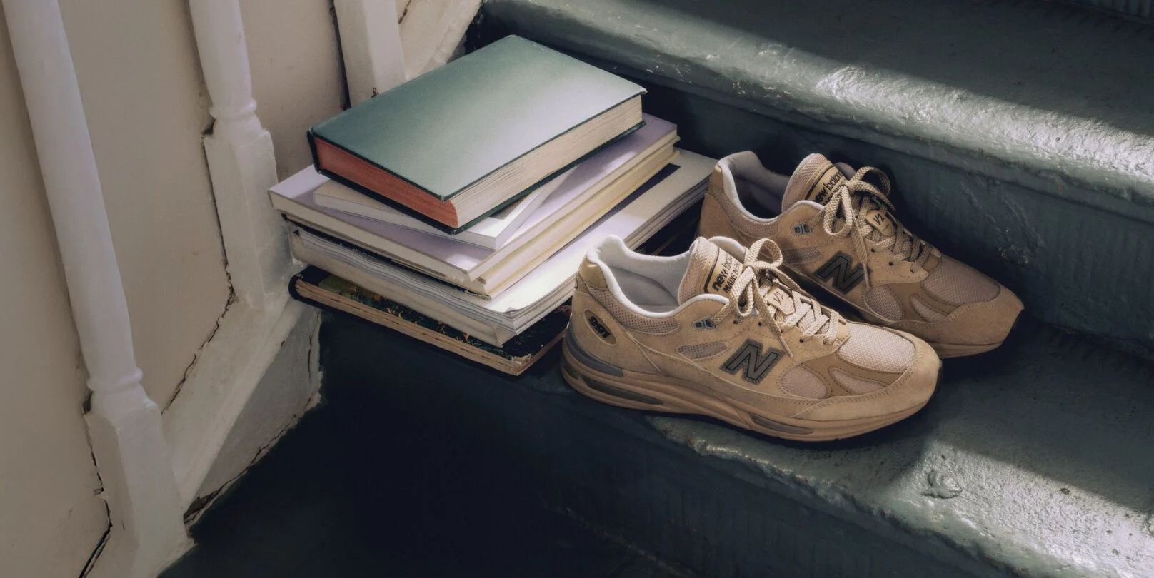 Une paire de chaussures sport New&nbsp;Balance Made in UK sur un escalier, &agrave; c&ocirc;t&eacute; d&rsquo;une pile de livres.