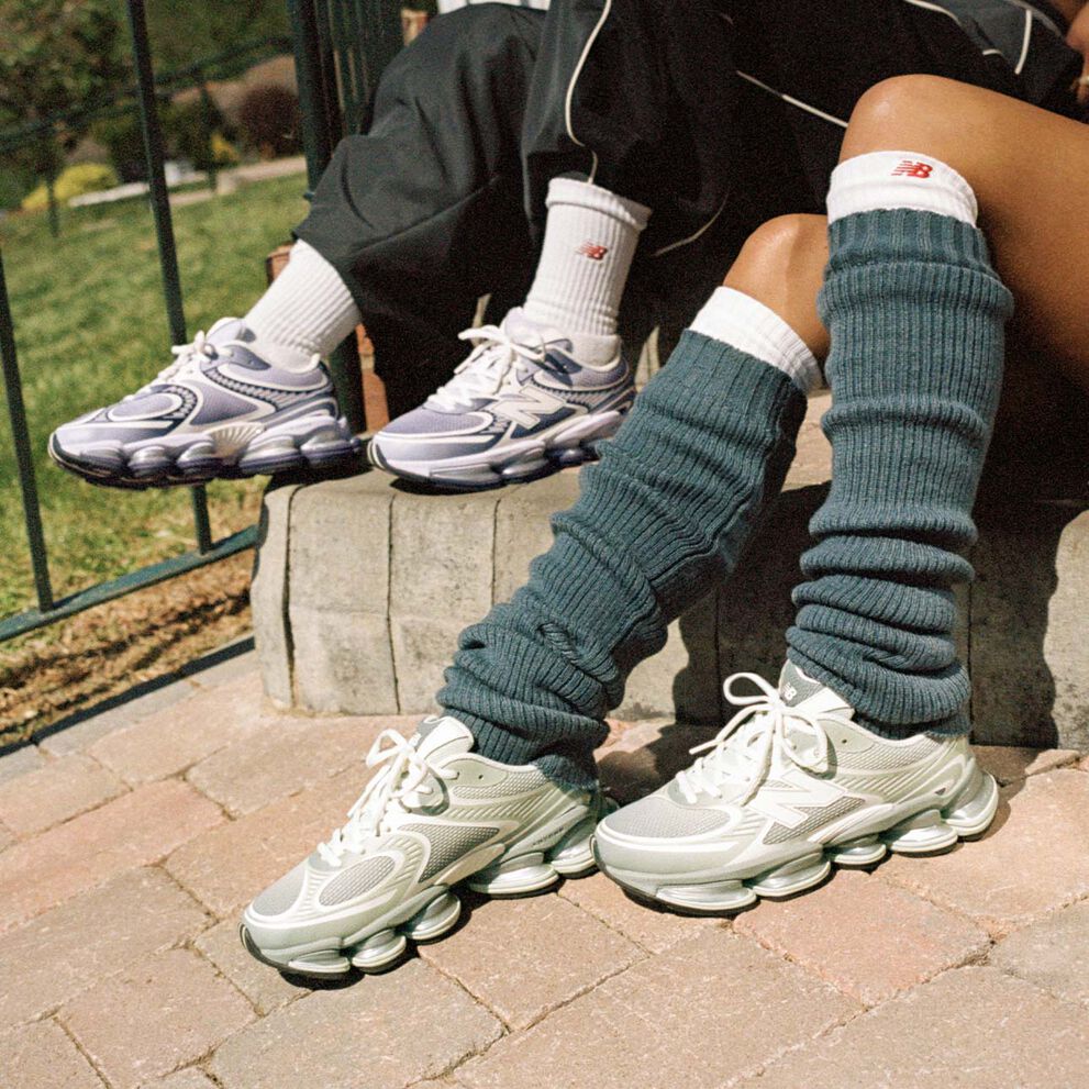 Deux personnes assises sur un trottoir portant des baskets New Balance.