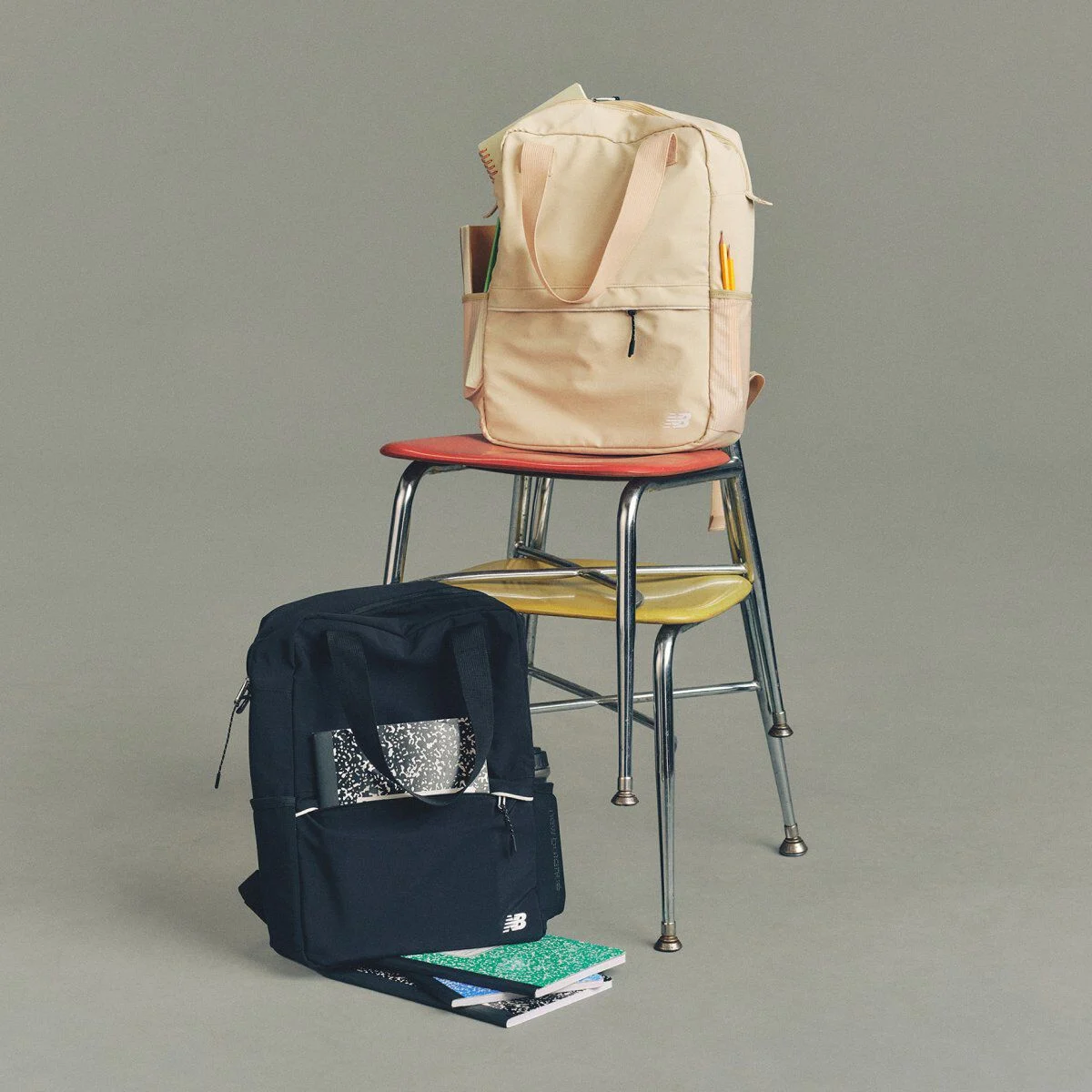 Image de studio d&rsquo;un sac &agrave; dos New Balance couleur cr&egrave;me et bleu marine pos&eacute; sur un tabouret en m&eacute;tal.