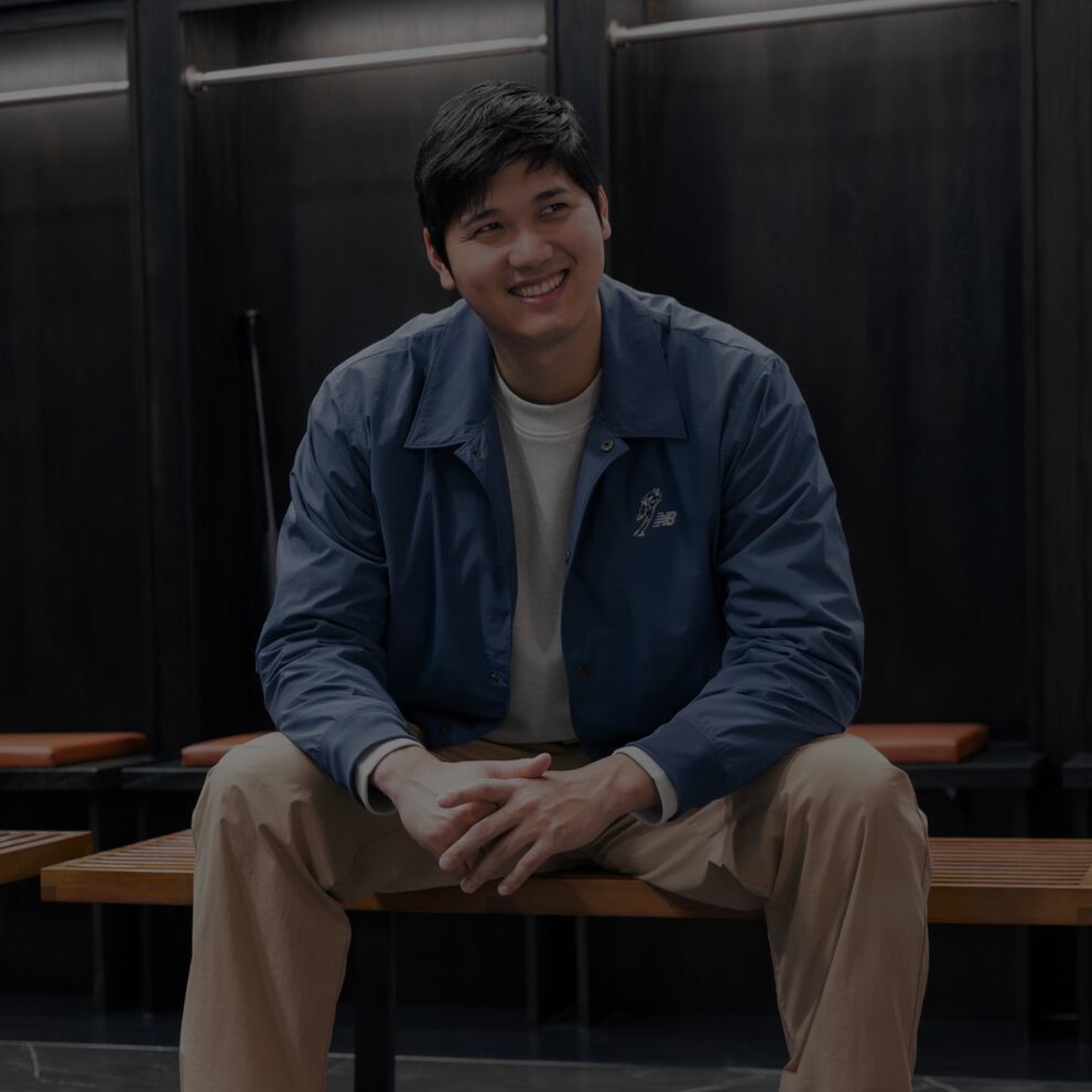 Shoehei Ohtani assis dans un vestiaire en veste bleue.