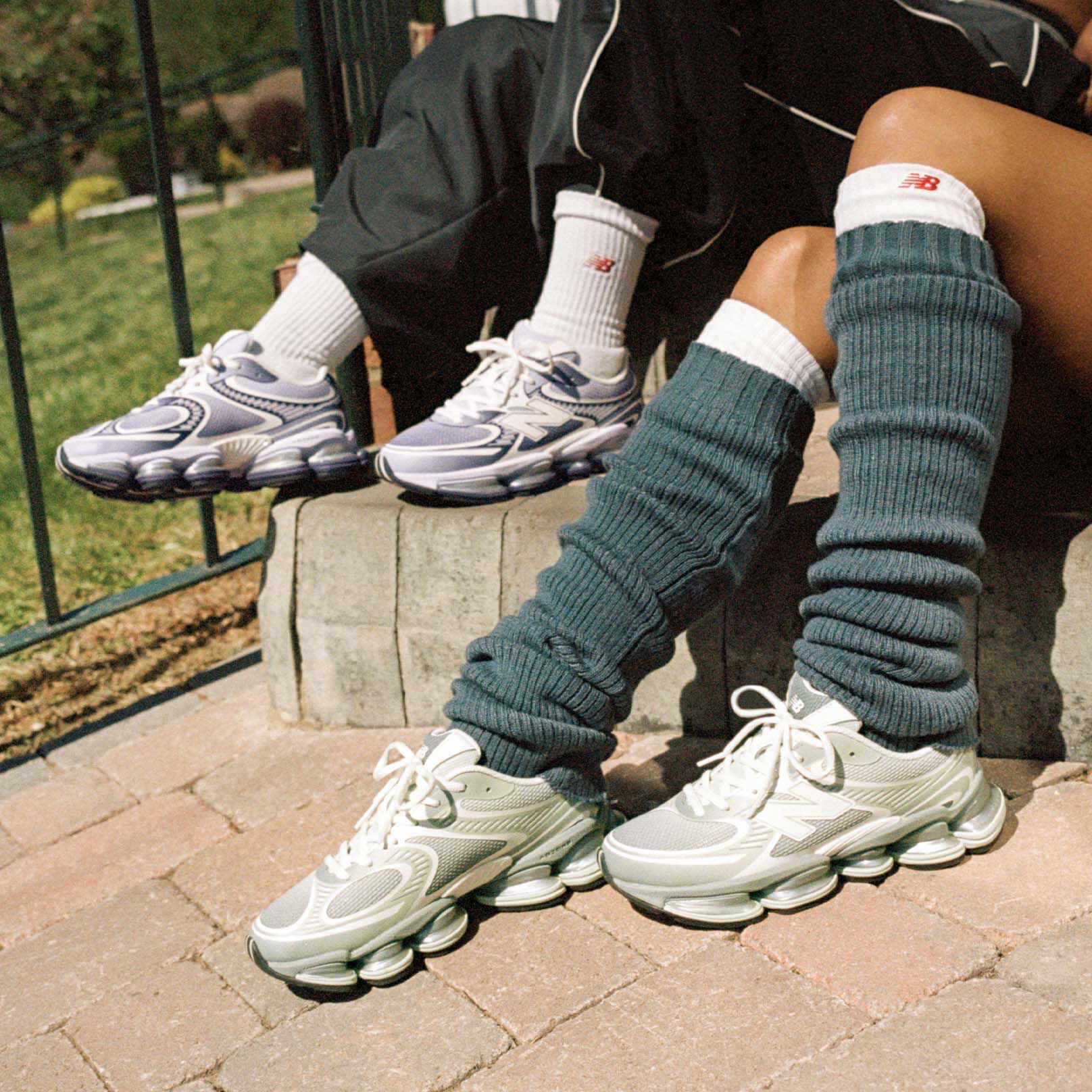 Deux personnes assises sur un trottoir portant des baskets New Balance.