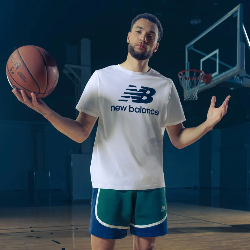 Zach wearing a white NB logo shirt holding a ball with his arms spread outward.