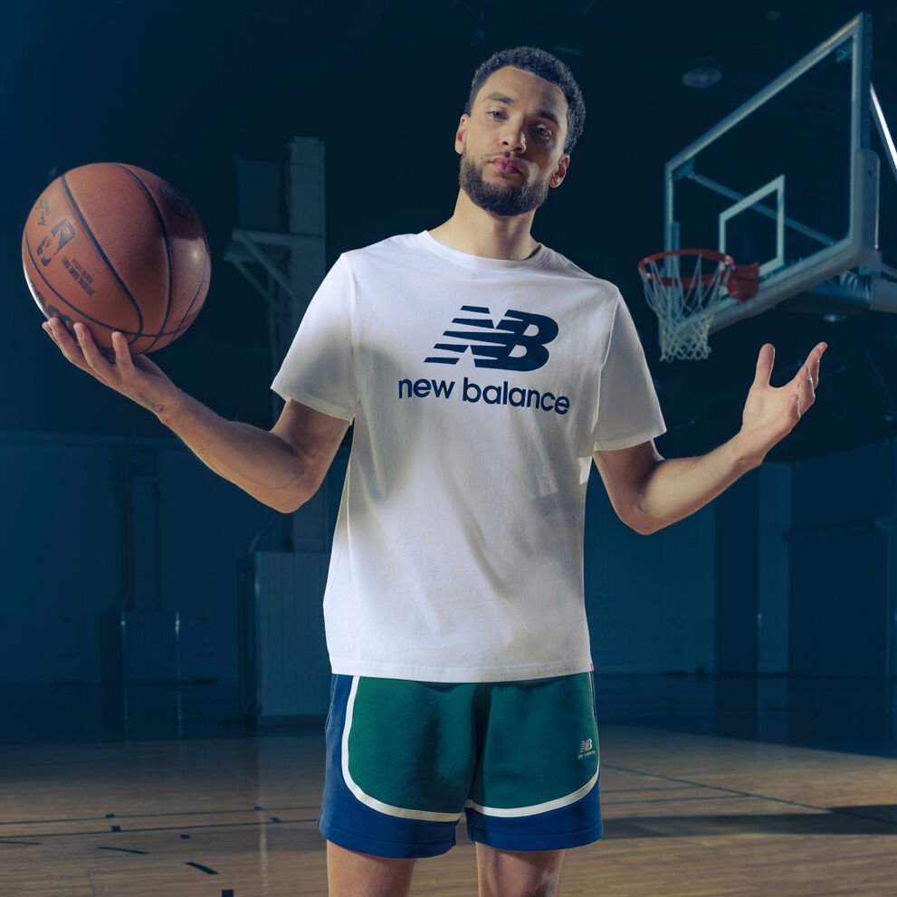 Zach wearing a white NB logo shirt holding a ball with his arms spread outward.