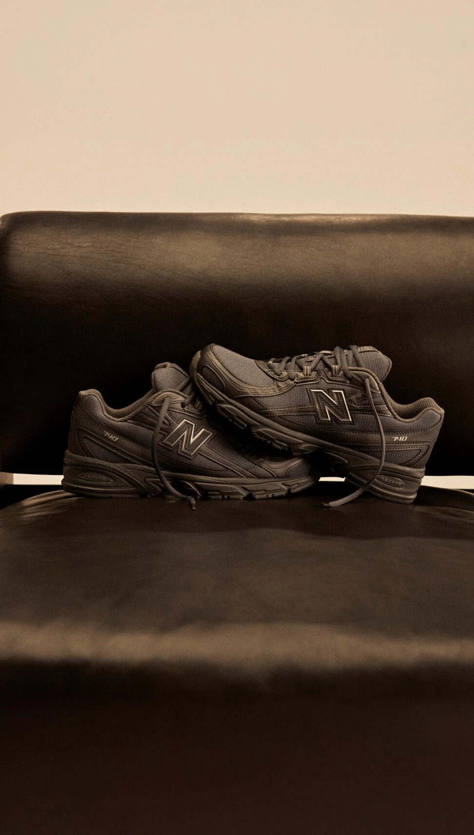 Dark New Balance 740 shoes on top of a dark leather and wooden chair.