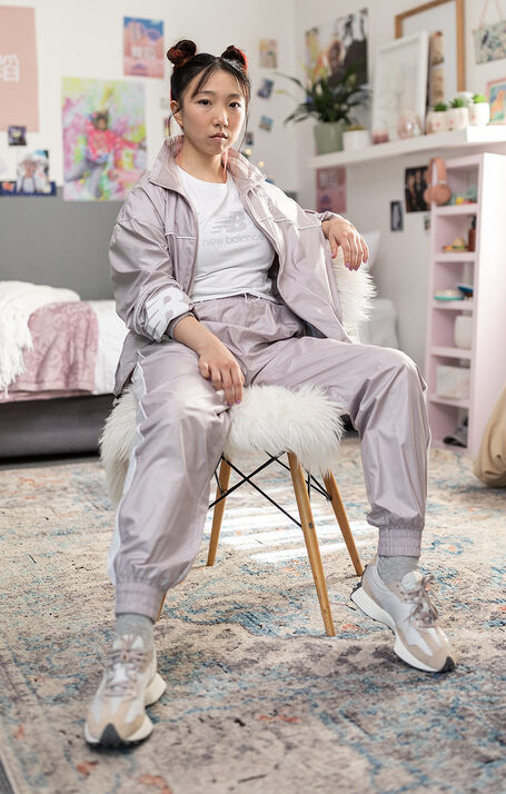 A teenage girl wearing a light grey NB track suit tying her NB 237 sneakers in her bedroom