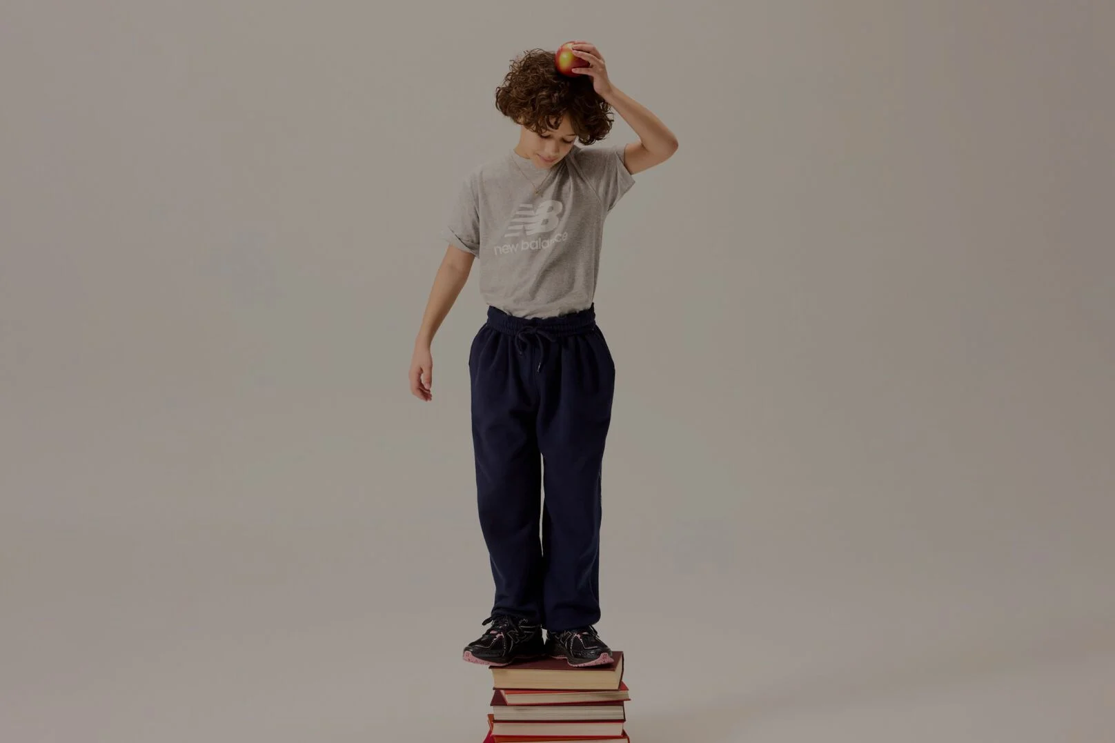 Kid standing on books holding an apple over his head.